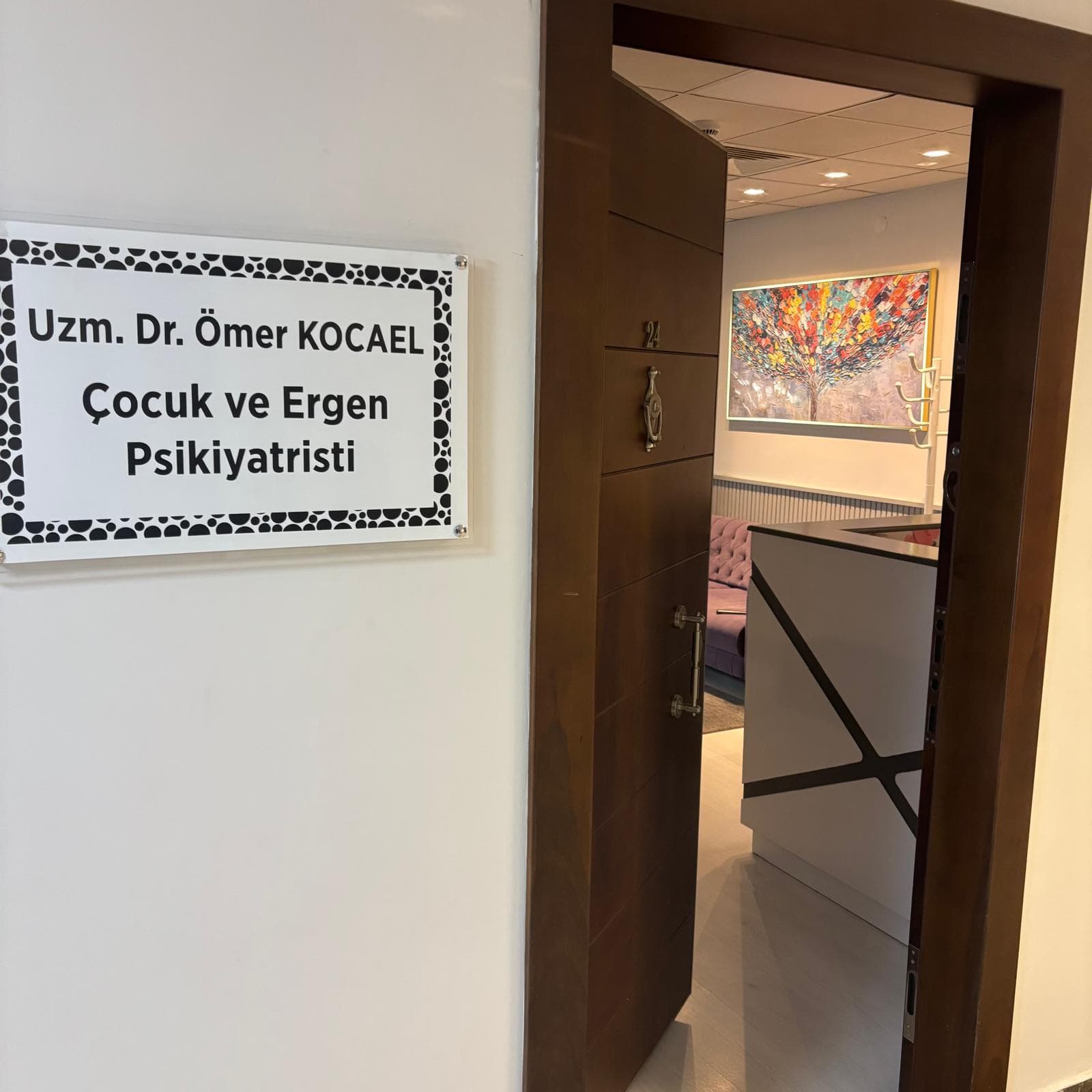 Umi Plaza 3. kattaki 24 numaralı kapı ve yanında “Uzm. Dr. Ömer Kocael, Çocuk ve Ergen Psikiyatristi” tabelası